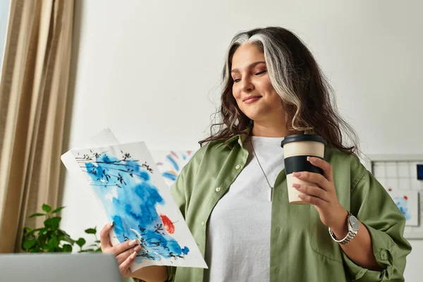 A joyful woman admires her artwork while sipping coffee in her stylish home. — Stock Photo