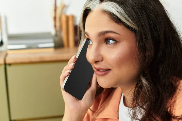 Una donna con un caratteristico ciuffo bianco sorride mentre parla al telefono a casa. — Foto stock