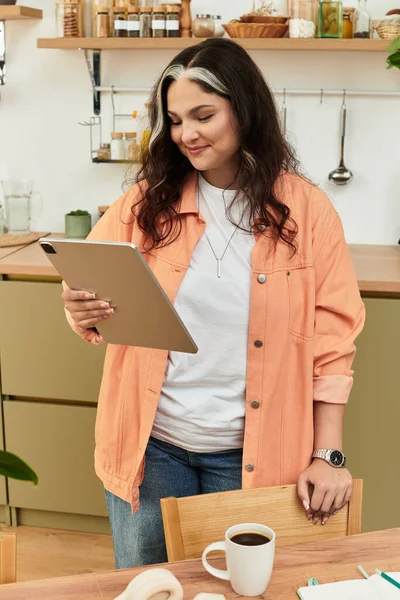 A woman with a unique white forelock relaxes in her stylish apartment while using a tablet. — Stock Photo