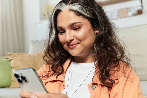 A woman with Waardenburg syndrome enjoys a moment at home looking at her smartphone and smiling. — Stock Photo
