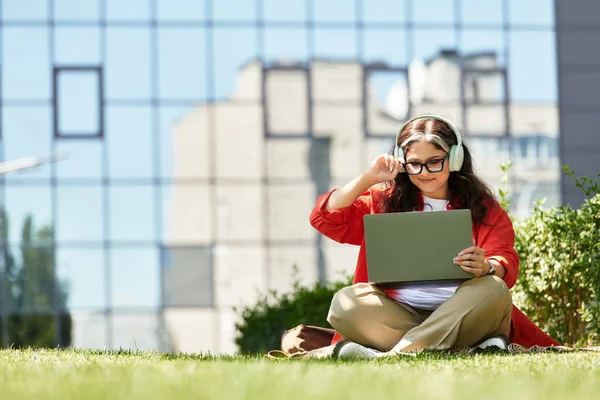 Woman with white forelock and blue eyes sits on grass, engaged with her laptop outside. — Stock Photo