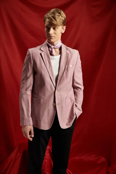 Молодий, красивий чоловік впевнено стоїть у спеціальному блістері, встановленому на яскравому червоному тлі. — стокове фото