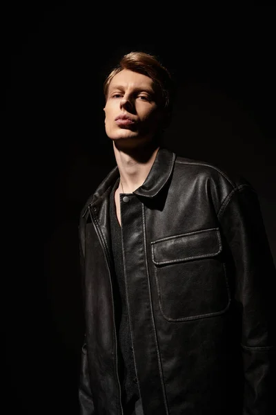 Молодий чоловік виражає привабливість і впевненість у шкіряній куртці на темному тлі. — стокове фото