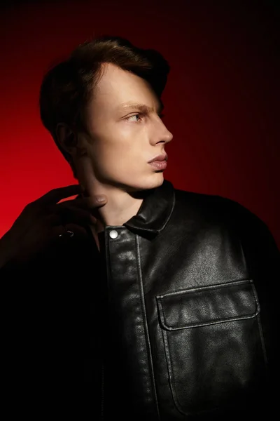 Молодий чоловік виявляє привабливість і силу на тлі яскраво-червоного фону, демонструючи сучасну мужність. — стокове фото