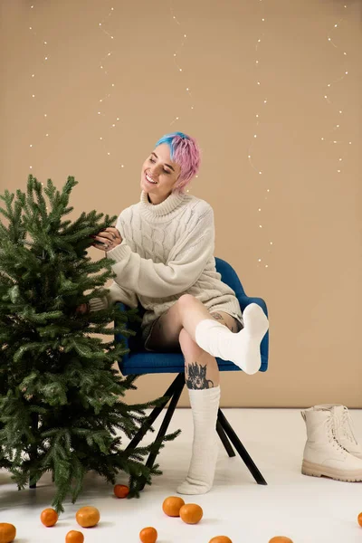 A beautiful young woman enjoys decorating a festive winter scene while sitting on a blue chair. - foto de stock