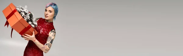 A beautiful young woman with colorful hair celebrates winter by holding a festive gift box. — Stockfoto