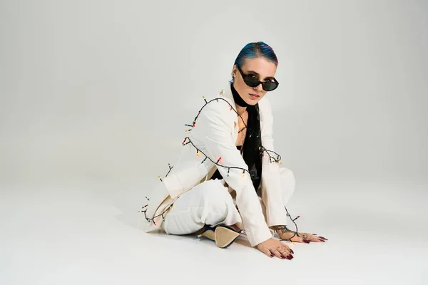 A young woman exudes winter cheer while playfully adorned with festive lighting, showcasing style. — Stockfoto