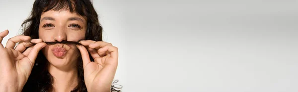 Eine schöne junge Frau hält ihre Haare an die Lippen und drückt in einem stylischen Outfit spielerischen Charme aus. — Stockfoto