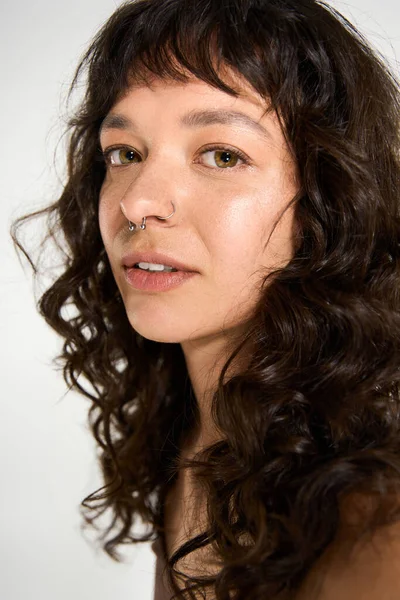 Selbstbewusste junge Frau mit lockigem Haar im trendigen Outfit vor neutralem Hintergrund. — Stockfoto