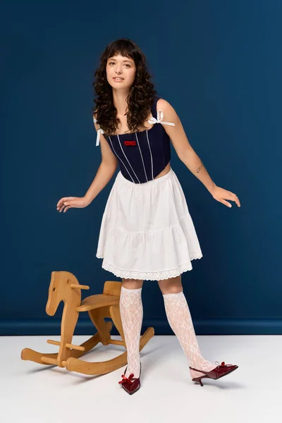 Frau im modischen Outfit steht neben einem hölzernen Schaukelpferd und zeigt ihren verspielten Geist. — Stockfoto