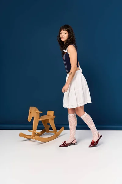 Молодая, элегантная женщина радостно играет с деревянным качающимся конём, обнимая свою игривую сторону. — стоковое фото