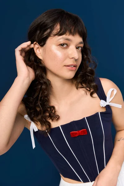 Frau mit lockigem Haar präsentiert trendiges Outfit und fesselnden Ausdruck im Studio-Setting. — Stockfoto