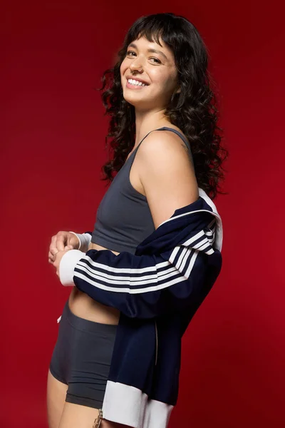 Frau im trendigen Outfit posiert warm, strahlt Freude und Stil vor rotem Hintergrund aus. — Stockfoto