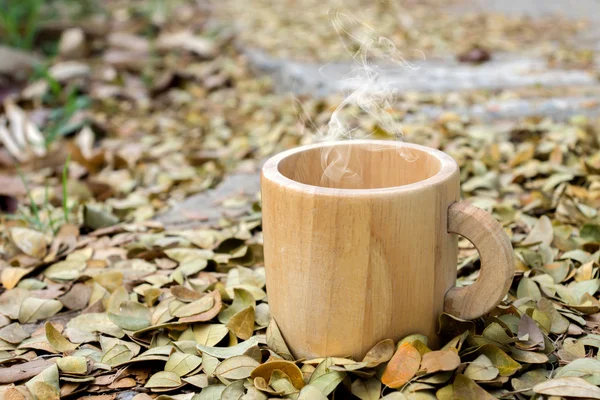 Houten koffiekopje op de grond met droge bladeren van de boom van de regen. — Stockfoto