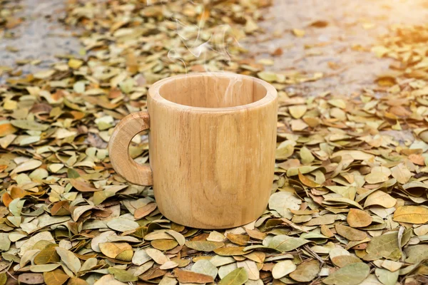 Xícara de café de madeira no chão com folhas secas da árvore de chuva . — Fotografia de Stock