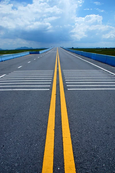 Άδειο δρόμο και τις γραμμές κίτρινο κυκλοφορίας με σύννεφα. — Φωτογραφία Αρχείου