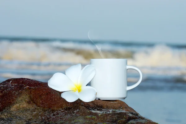 在海滩上的咖啡杯子和鸡蛋花鲜花 — 图库照片