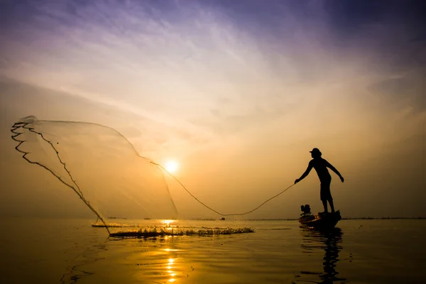 Silhouettes pêcheur jetant des filets de pêche au coucher du soleil . — Photo