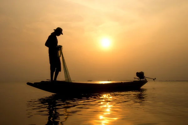 Silhuetas pescador jogando redes de pesca durante o pôr do sol . — Fotografia de Stock