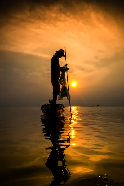 Siluetas pescador lanzando redes de pesca durante la puesta del sol . — Foto de Stock