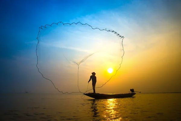 Silhuetter fisherman kasta fiskenät under solnedgången. Stockbild