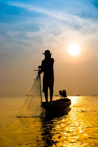 Silhuetter fisherman kasta fiskenät under solnedgången. Stockbild