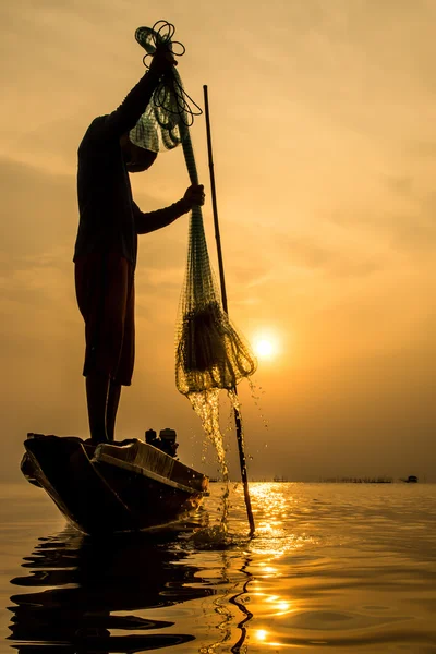 Silhuetter fisherman kasta fiskenät under solnedgången. Stockbild