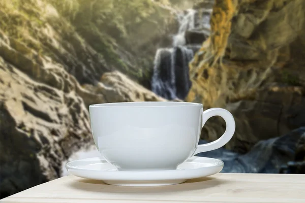 Copo de café branco com borrão de fundo de rocha e cachoeira . — Fotografia de Stock