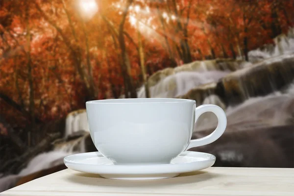 White coffee cup with blur of autumn forest and waterfall backgr — Stock Photo, Image