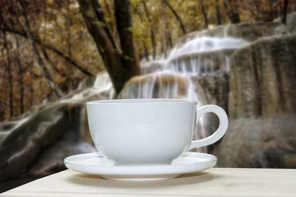 Vit kaffekopp med oskärpa av hösten skogen och vattenfall bakgrunds — Stockfoto