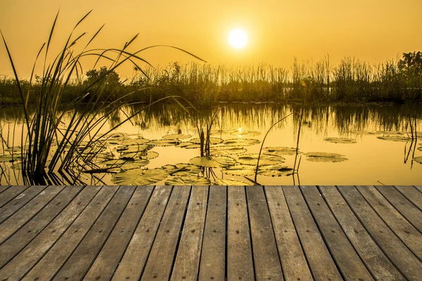 Holzsteg mit einem Hintergrundbild des Sees bei Sonnenuntergang. — Stockfoto