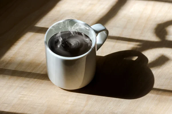 Iluminação da janela com xícara de café branco quente na madeira . — Fotografia de Stock