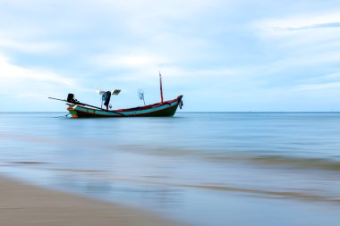 Mavi gökyüzü ve kum ile sahildeki balıkçı teknesi.