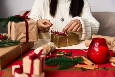 Eller, evde neşeli bir bayram kutlaması için güzelce paketlenmiş bir hediyeyi dikkatlice süslüyor..