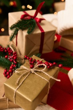 Altın ve kahverengiye sarılı dekoratif Noel hediyeleri şenlikli yeşillikler ve kırmızı böğürtlenler arasında oturur..