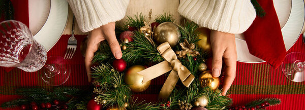 Руки готовят праздничный рождественский венок из золота и красных украшений.
