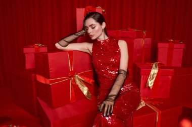 Zarif kırmızı elbiseli genç bayan renkli hediyeler arasında neşeli bir tatil atmosferinin tadını çıkarıyor..