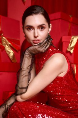 Parlak kırmızı elbiseli genç ve güzel bir kadın canlı bayram hediyeleri arasında zarifçe poz veriyor..