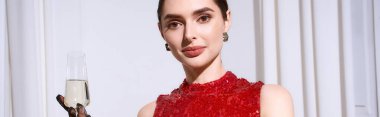 Şenlikli atmosferde zarif giyinmiş ve elinde bir kadeh şampanya tutan genç bir kadın var..