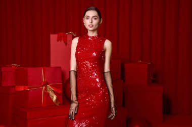 Parlak giyimli genç bir kadın kutlama sırasında neşeli kırmızı hediyeler denizinde neşe saçıyor..