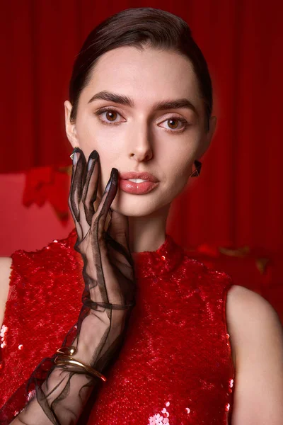 Işıldayan kırmızı elbiseli genç bir kadın canlı bir şenlik ortamında zarifçe poz veriyor..