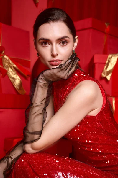 Parlak kırmızı elbiseli genç ve güzel bir kadın canlı bayram hediyeleri arasında zarifçe poz veriyor..