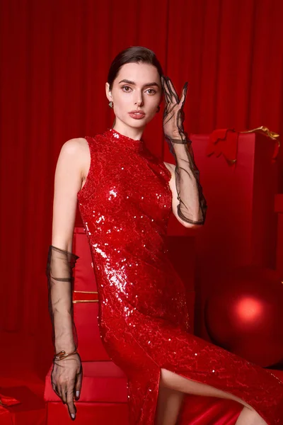 Genç bir kadın kırmızı pullu bir elbise içinde ışıldıyor, şenlikli ruhu zarafetle kucaklıyor..