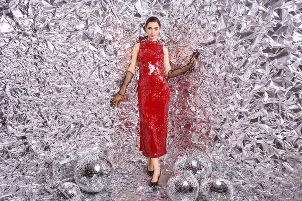 Şenlikli kırmızı giyinmiş genç, güzel bir kadın ışıltılı bir kutlama ortamında sevinçle poz veriyor..