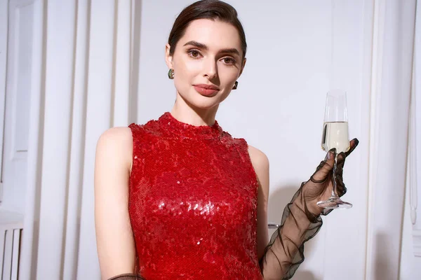 Şenlik kıyafetleri içinde güzel genç bir kadın bir kutlama için bir bardak şampanya tutuyor..