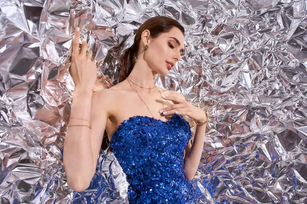 Göz kamaştırıcı genç bir kadın ışıldayan metalik bir arka plana karşı şenlikli bir moda sergiliyor..