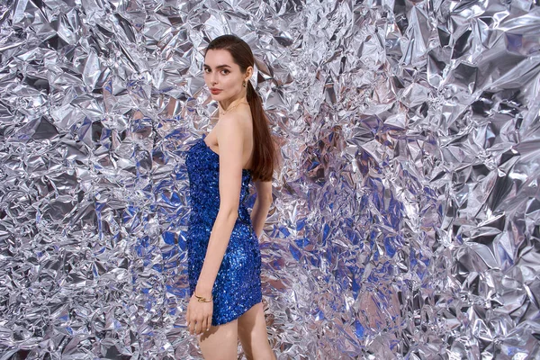 Güzel genç bir kadın parıldayan bir elbise içinde poz veriyor, canlı bir kutlama atmosferinin tadını çıkarıyor..