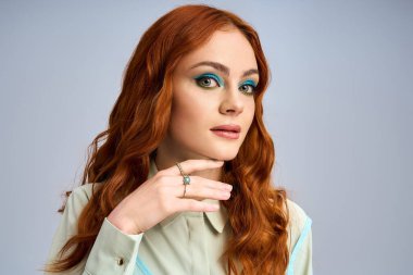 Göz alıcı kızıl saçlı genç bir kadın stüdyoda cesur, renkli göz makyajı yapıyor..