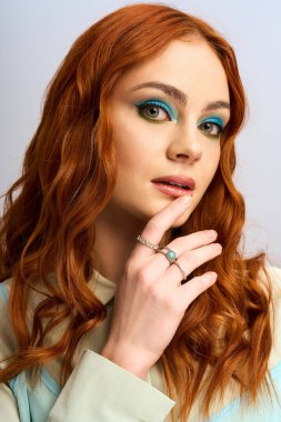 Genç bir kızıl, parlak bir stüdyoda poz verirken cesur göz makyajını gösteriyor..