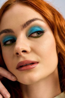 Genç bir kızıl, parlak bir stüdyoda poz verirken çarpıcı makyajını sergiliyor..